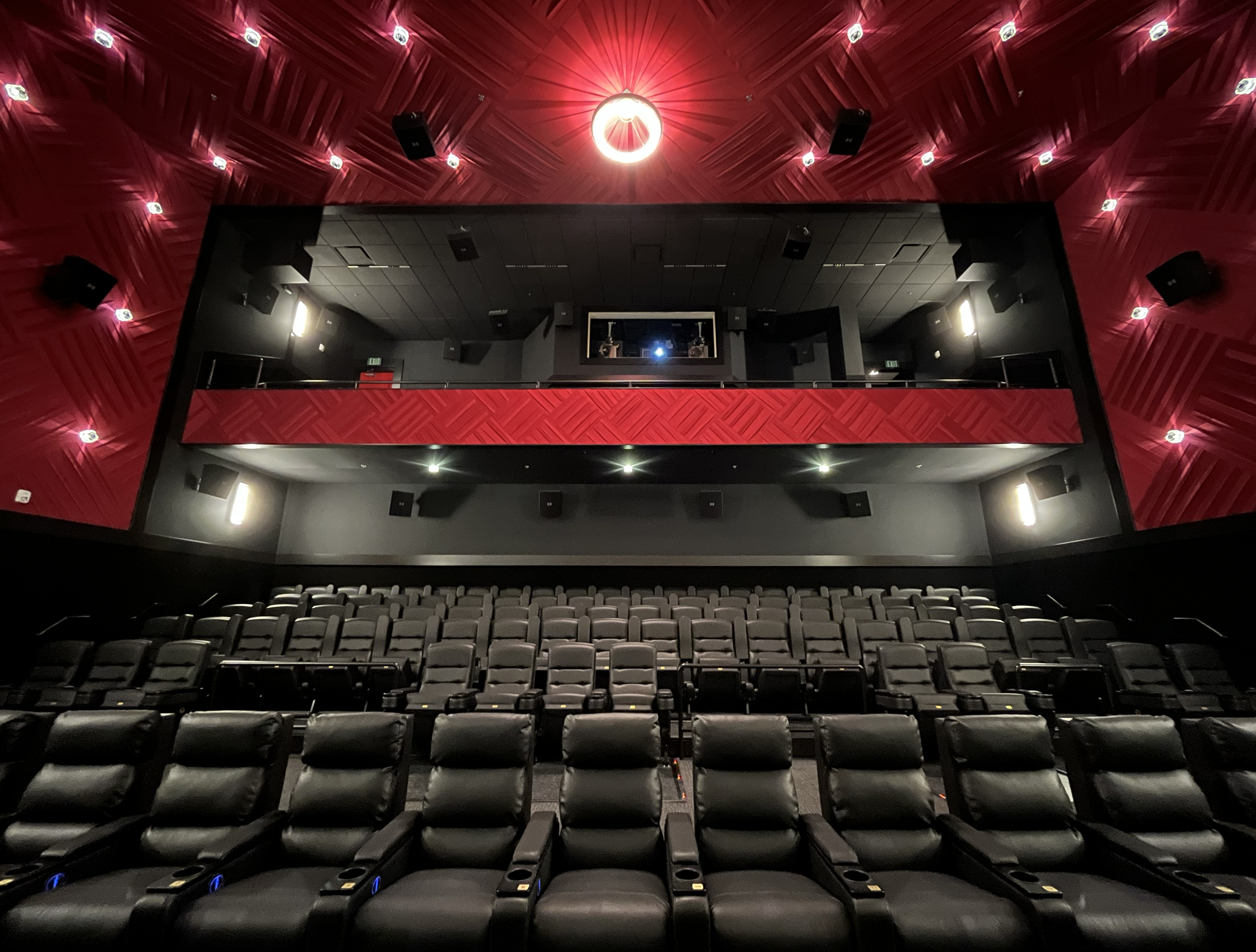 View of the back of a screening room with black theater seats and red overhead lighting