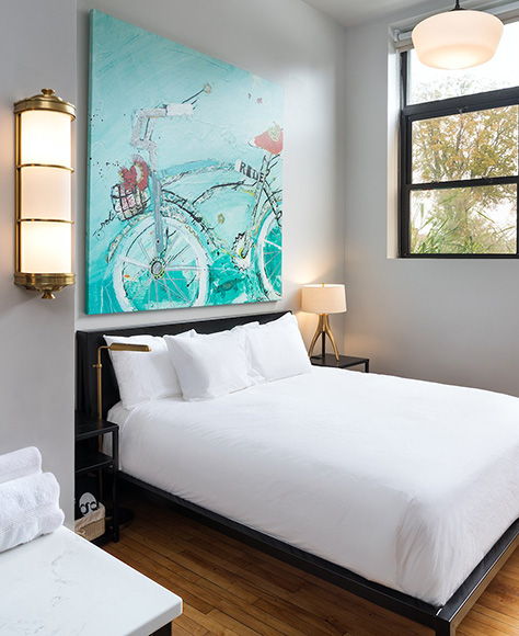 hotel bed with white sheets and bright painting hanging on the wall above
