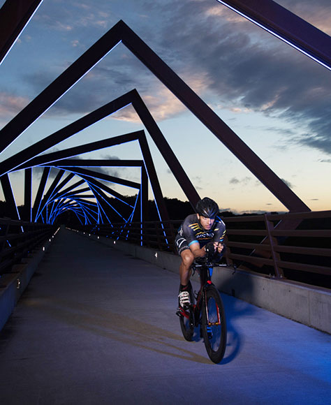 TJ Tollakson riding his bike across the Trestle Trail bridge at sunset.