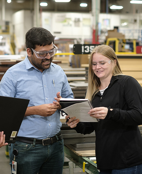 Woman and man standing together in an industrial setting looking together at a notebook.