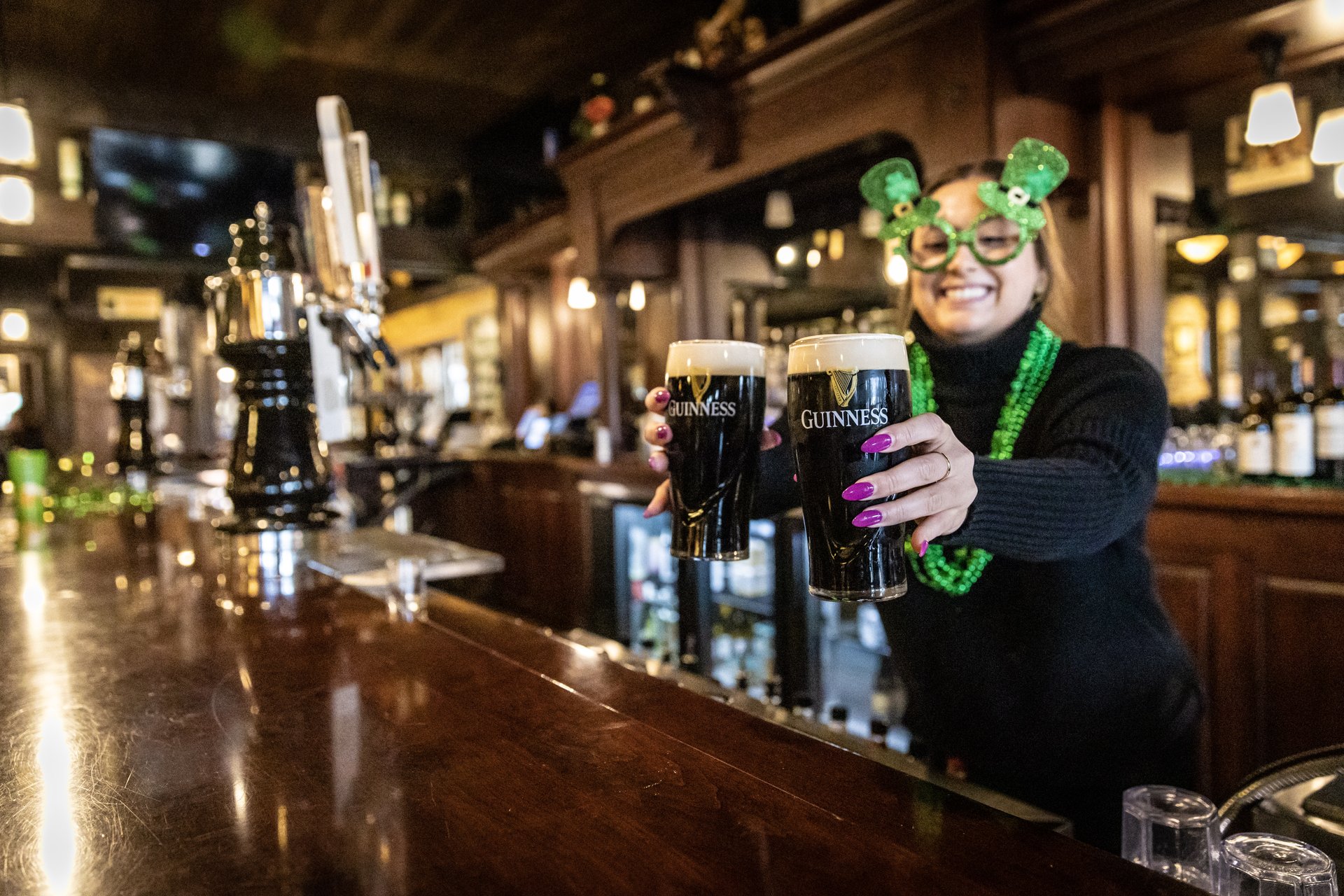 Bartender wearing St. Patrick's Day glasses serves two Guiness beers in Ames Iowa