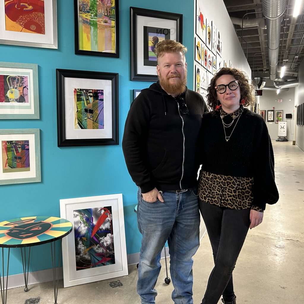 Sarah Booz and Kyle Kirwan standing in front of artwork displayed at Mainframe Studios