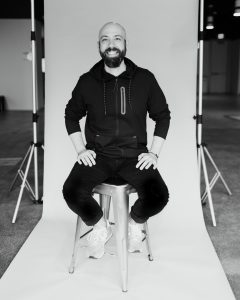 Ben Milne sitting on a stool in front of a picture backdrop.