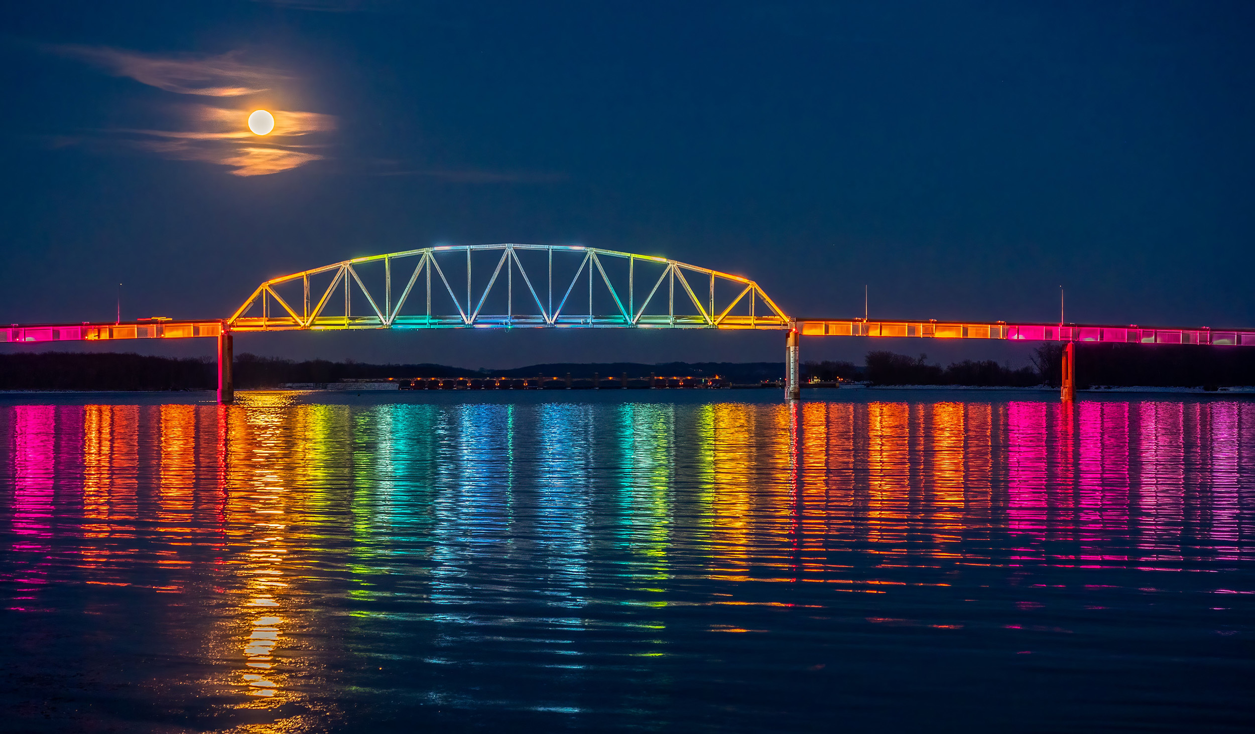 Bridge in Muscatine Iowa lit up with rainbow colors under a full moon