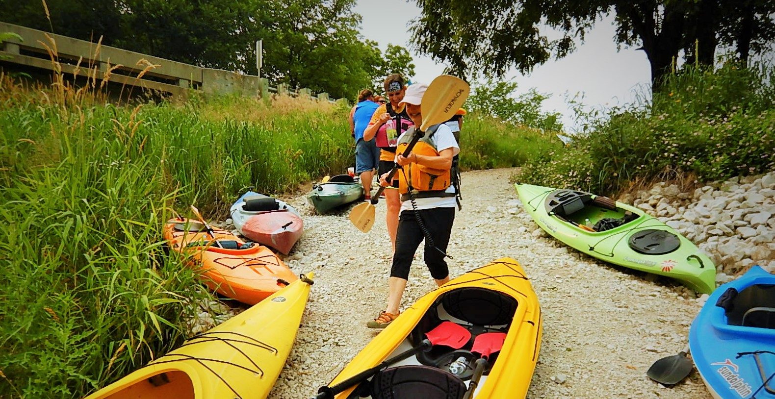 A group of people with life jackets and paddles standing by kayaks on the ground