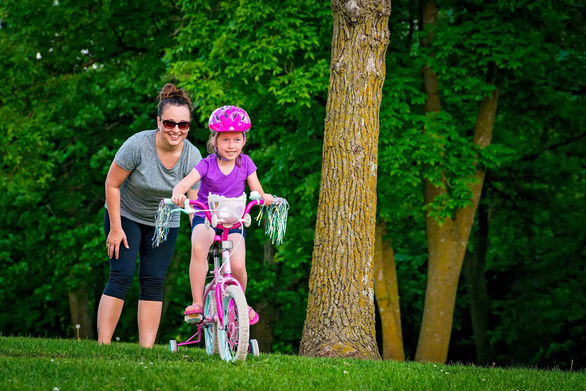 Mother sending behind her daughter as she rides away on her bike.