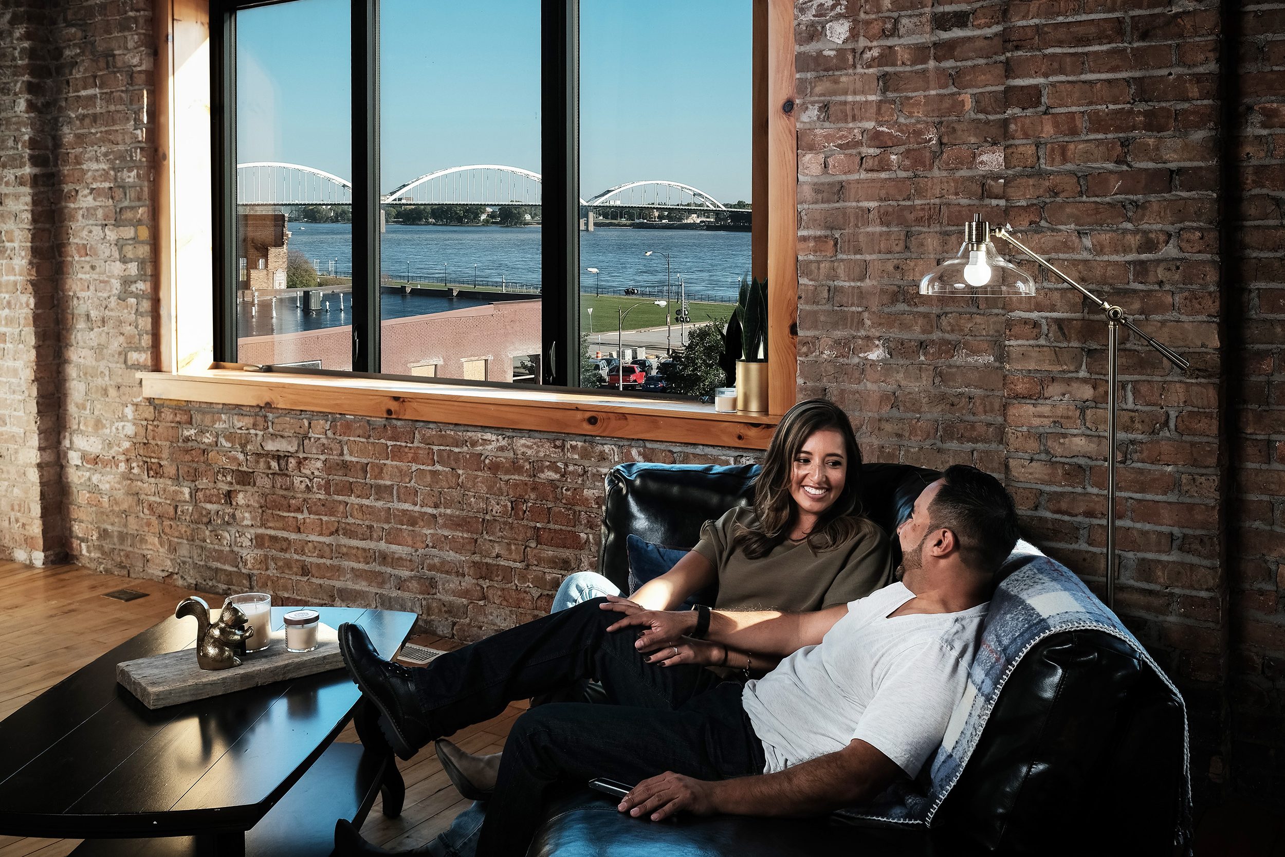 Couple sits on a couch in an apartment with a view of the Mississippi River outside the window