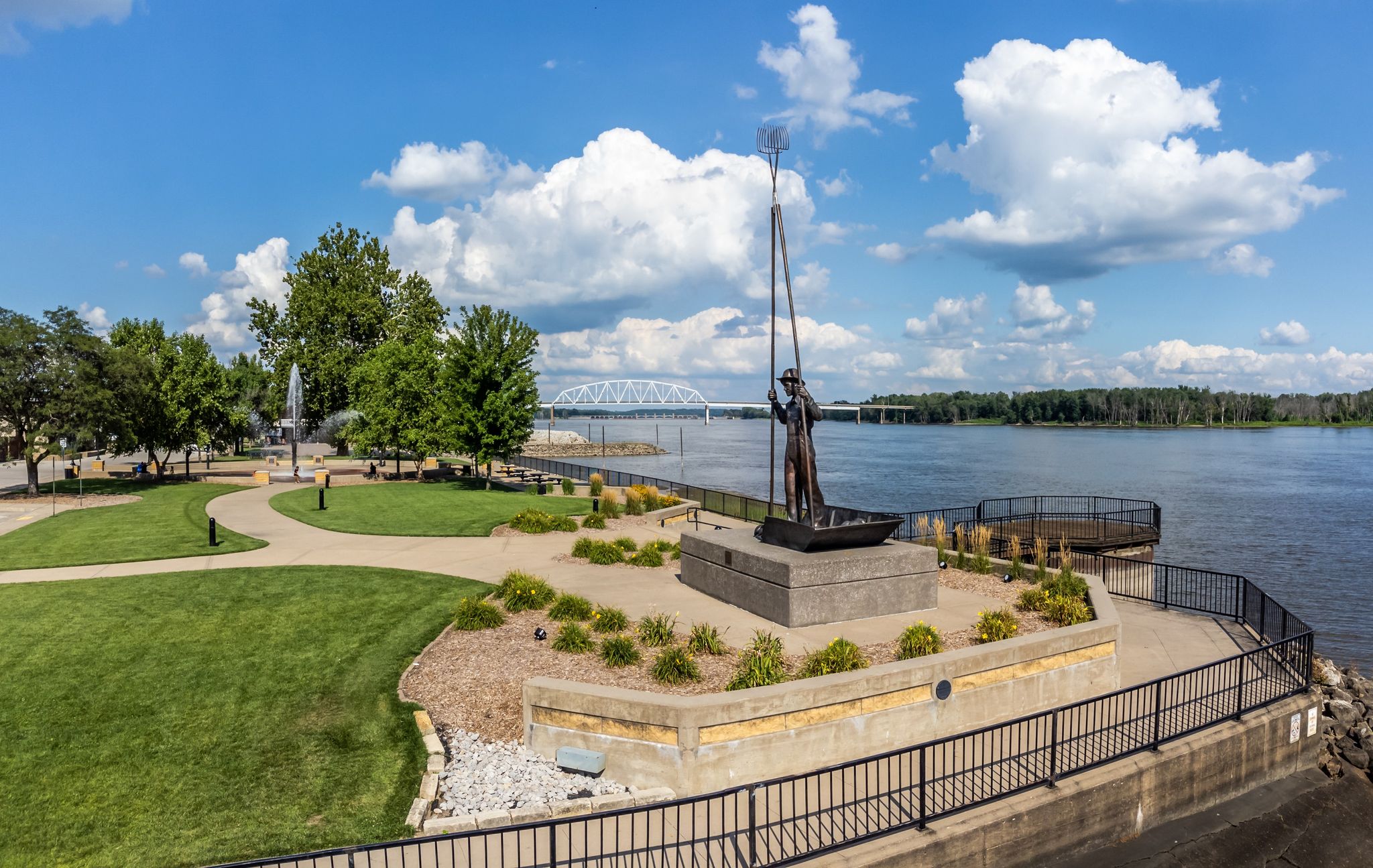 drone shot of riverfront with sculpture of a man and bridge in the background