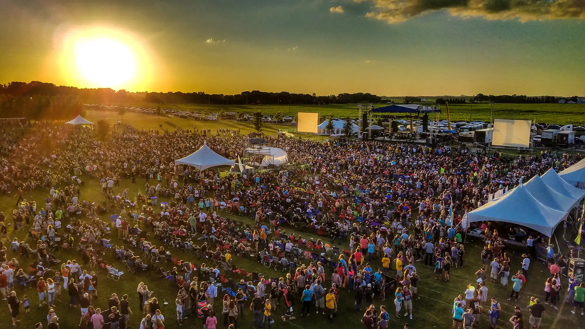 A large crowd of people at an outdoor festival during sunset