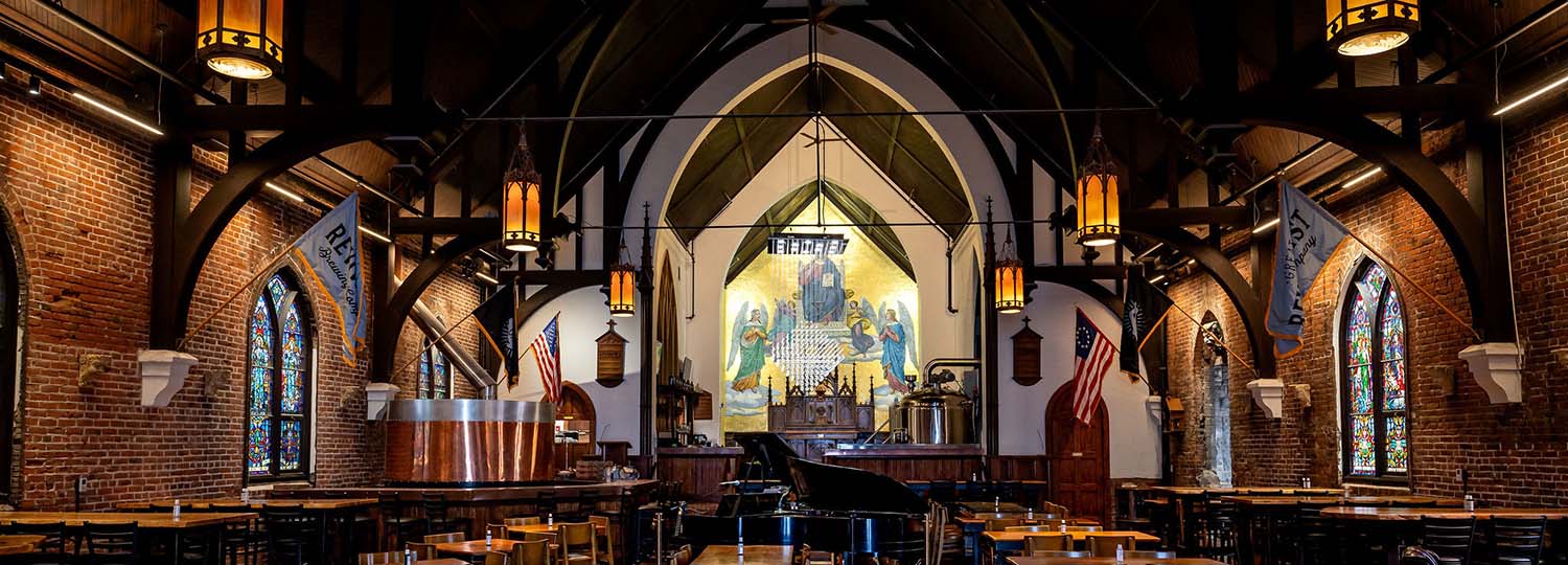 Great Revivalist Brewery interior view with old church pews, light fixtures, and stained glass windows.