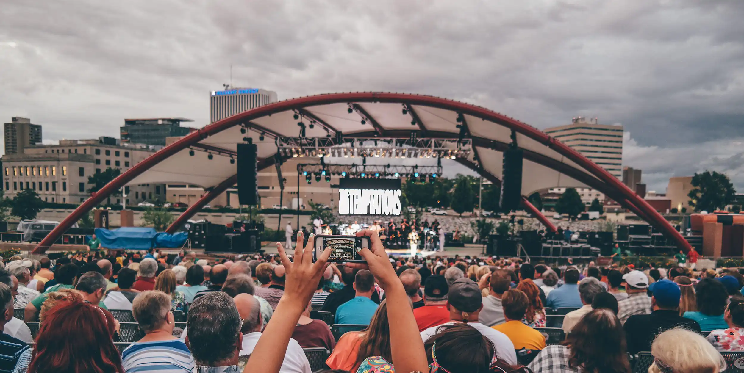 Woman in the audience at an outdoor concert takes a photo of the stage