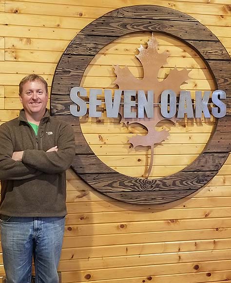 Joel Bryan standing in front of the Seven Oakes sign. 