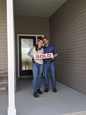 Tom and Maggie Gouger holding a SOLD sign outside their new home. 
