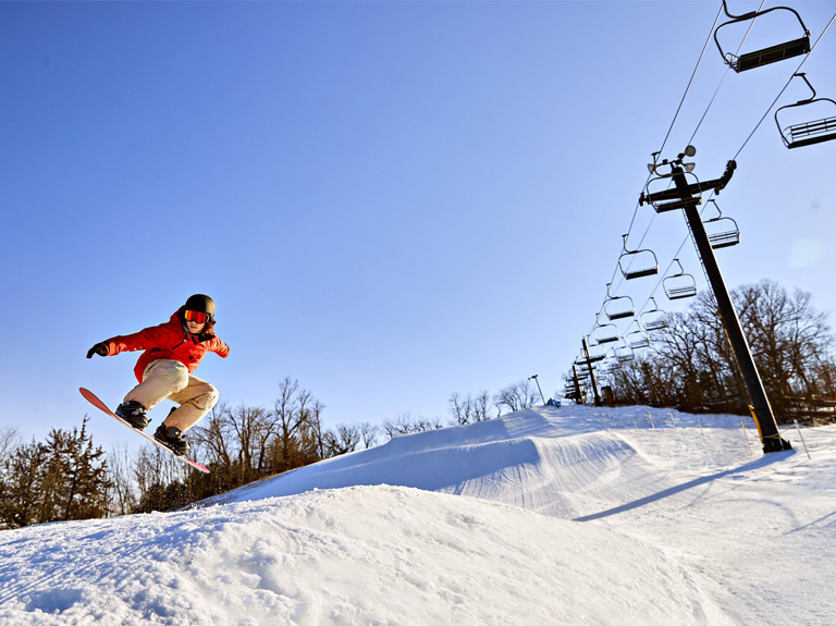 Snowboarder jumping a small hill on a ski slope.