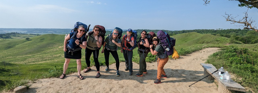 Group of women standing in a group with backpacks on.