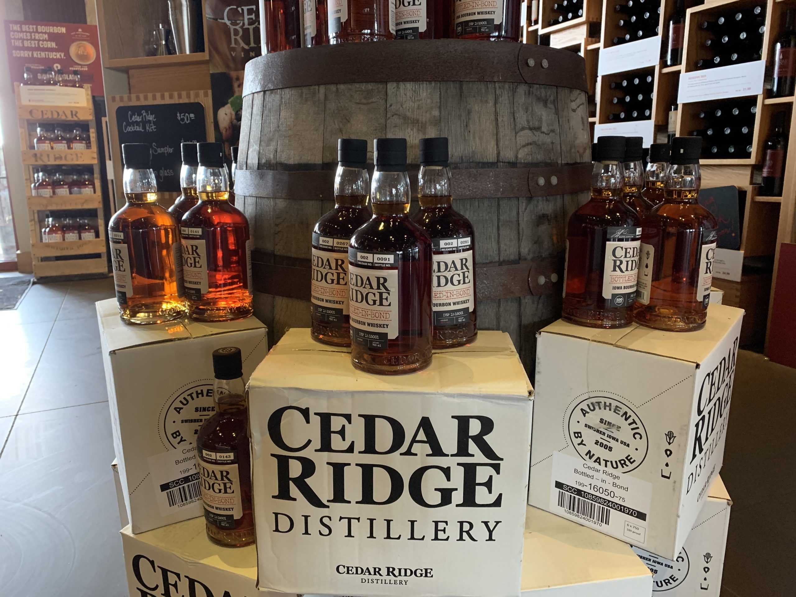 Cedar Ridge Distillery whiskey bottles sitting on top of branded boxes in front of an old whiskey barrel.