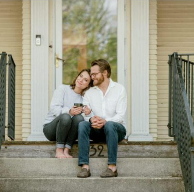 a man and a woman sit on the front porch of a yellow house