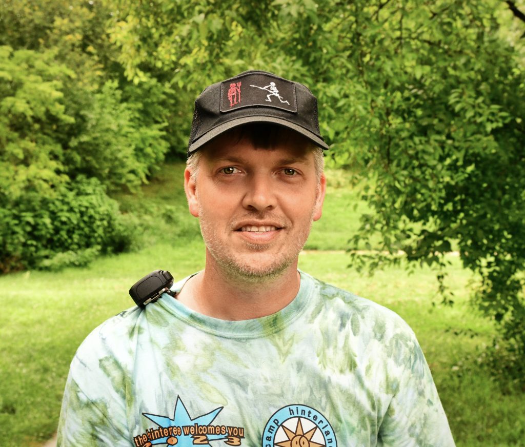 Sam Summers wearing a hat and green t shirt standing in a grassy area