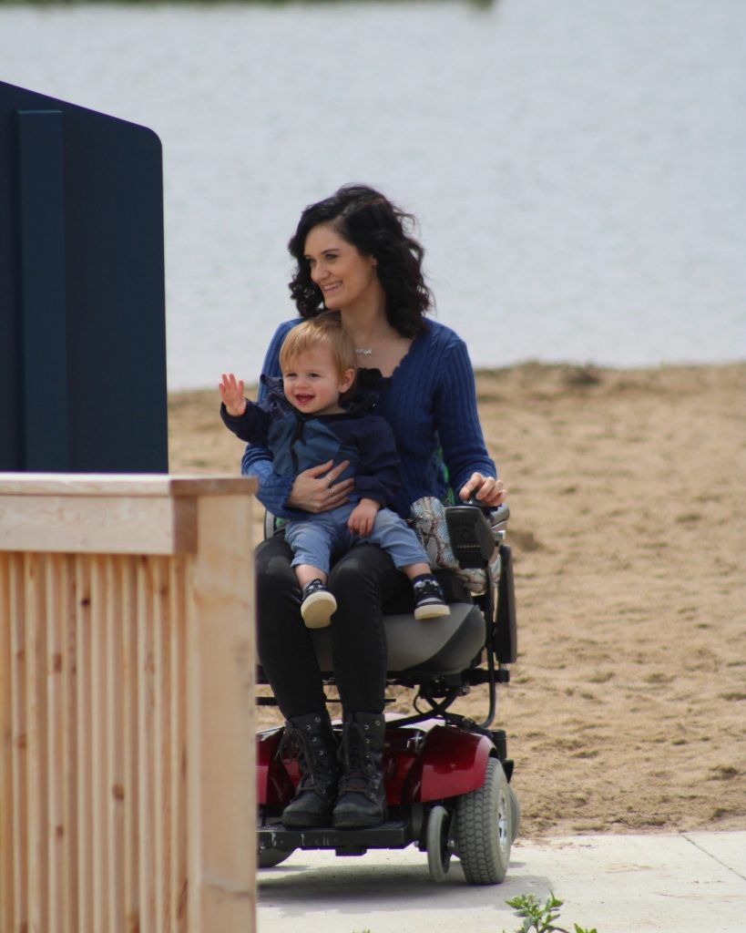 A woman in a wheelchair holds her young son on her lap.