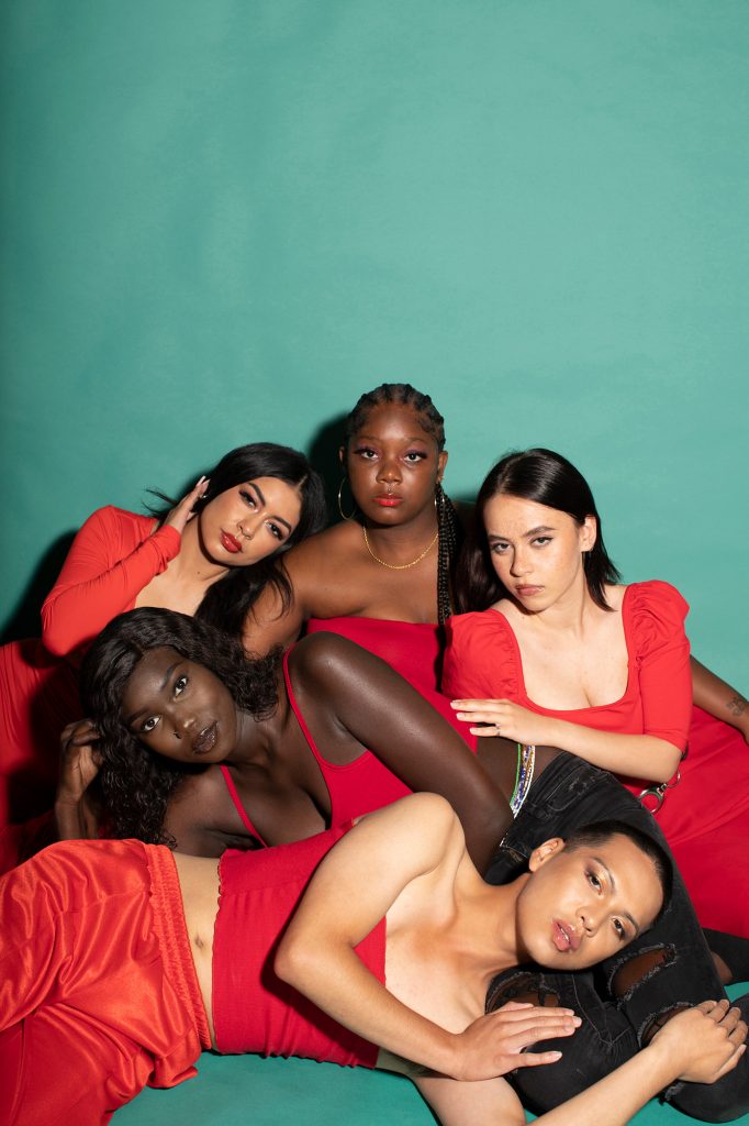 5 women wearing red and modeling lip gloss in front of a green background