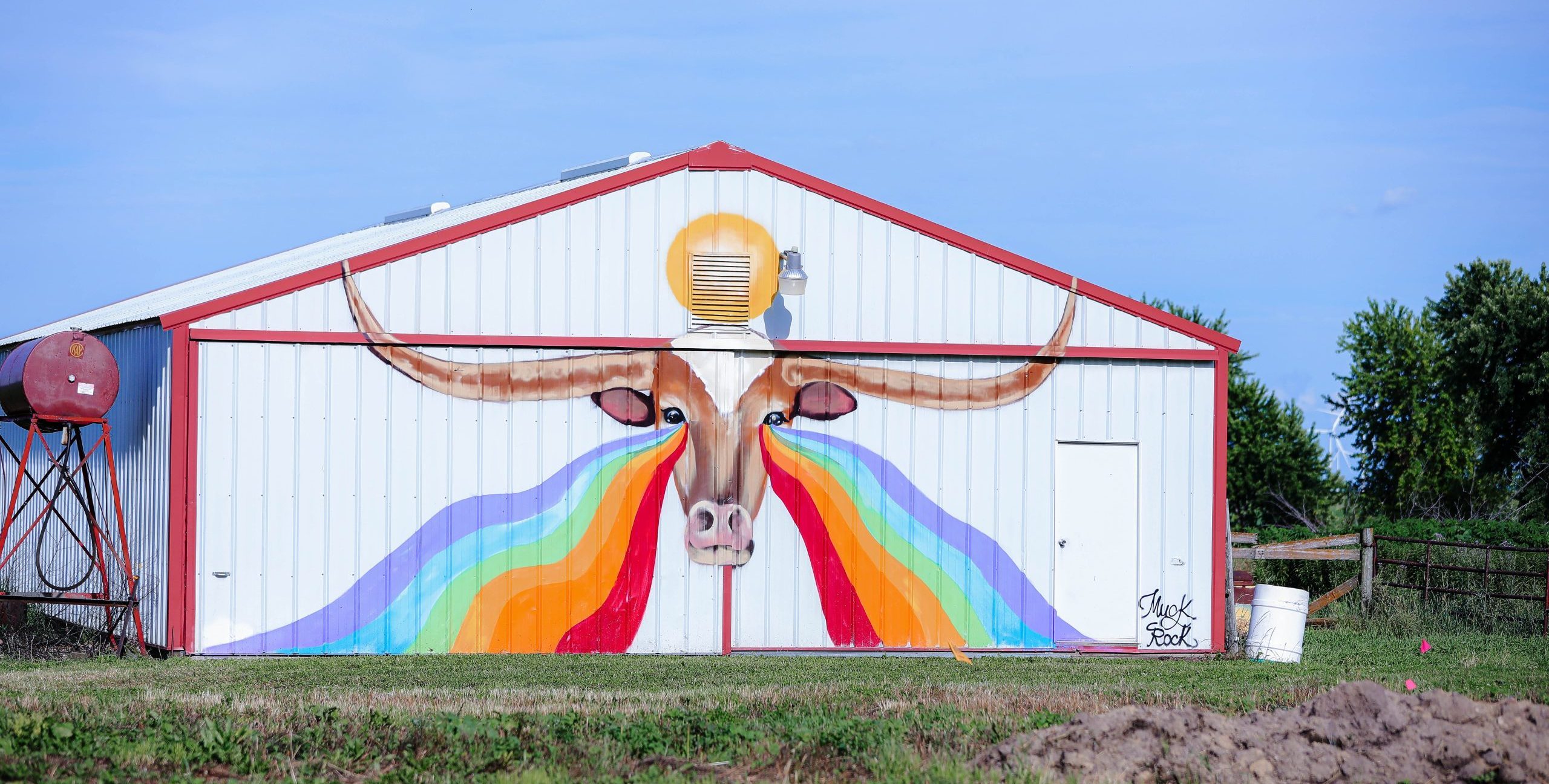 mural on a building features rainbow rivers pouring from the eyes of a Longhorn steer