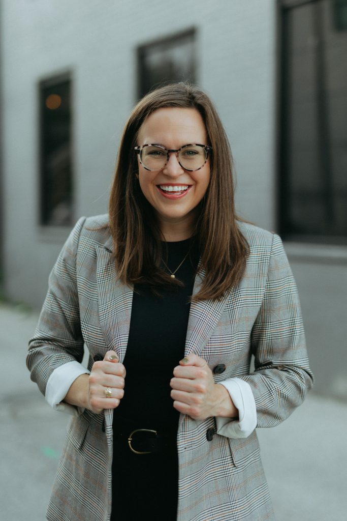 A women wearing a grey blazer smiles at the camera.