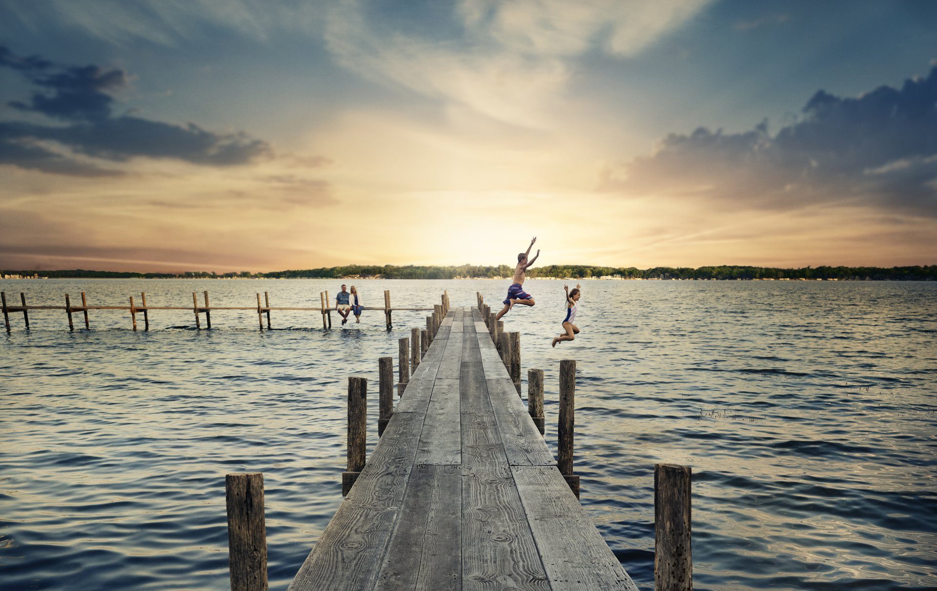 kids jumping off a dock at a lake during sunset